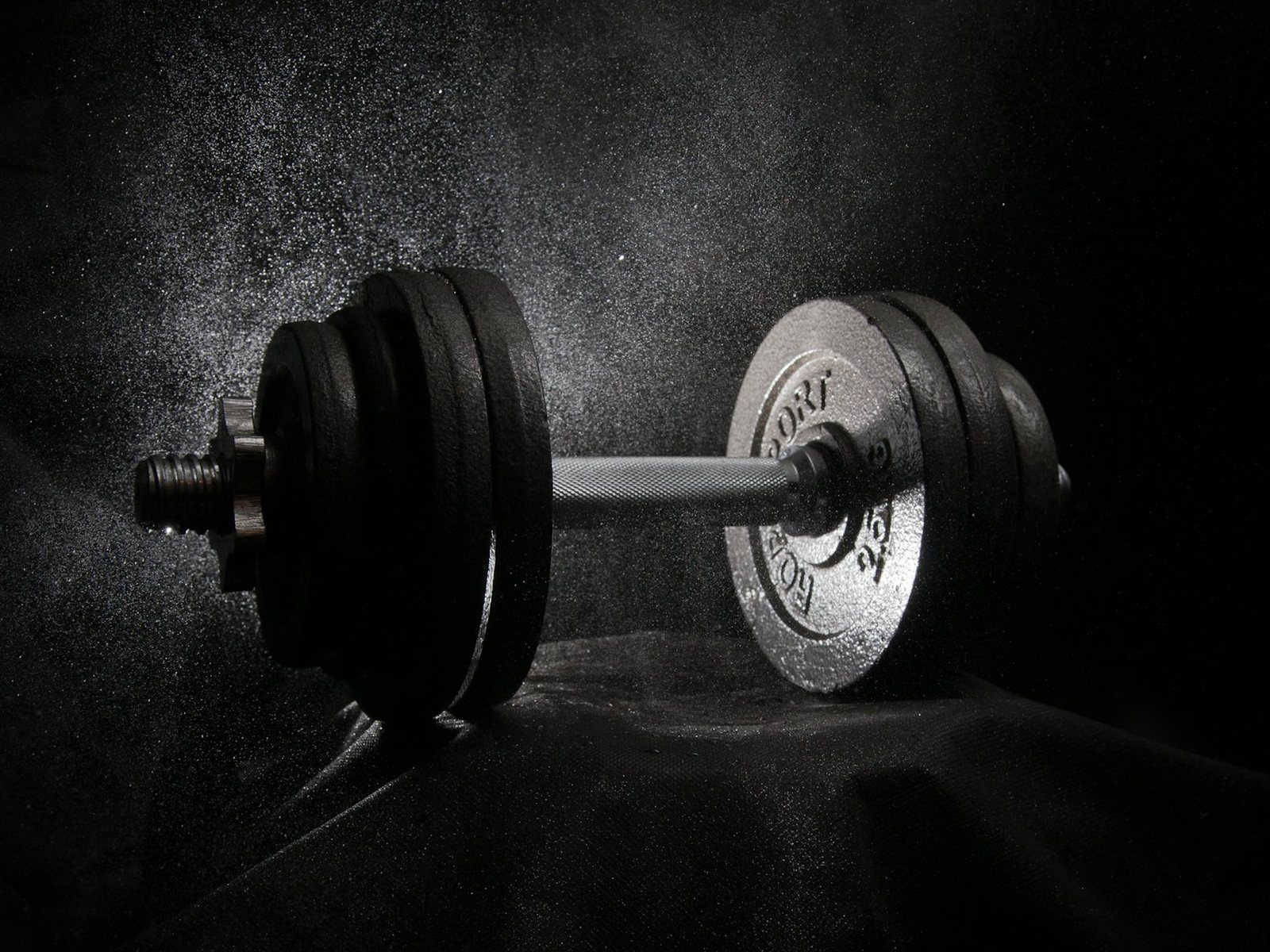 A loaded barbell on a dark floor with chalk dust in the air
