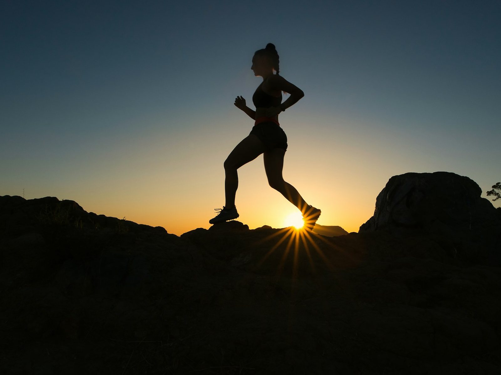 A runner in silhouette on a rocky ridge at sunrise